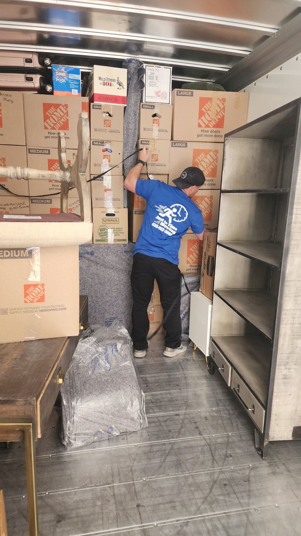 A mover in a branded shirt loading cartons and shelving into a moving truck