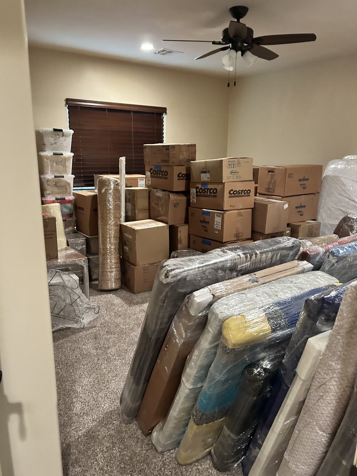 Stacked cartons and plastic-wrapped mattresses gathered in a room ready for loading