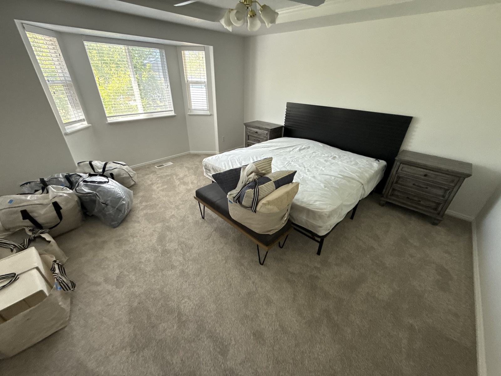 A bed frame and mattress set up in a bright bedroom with packed bags still to unpack