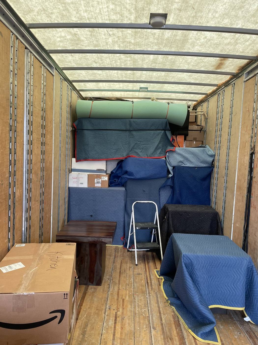 A moving truck interior neatly loaded with furniture protected in blue moving blankets