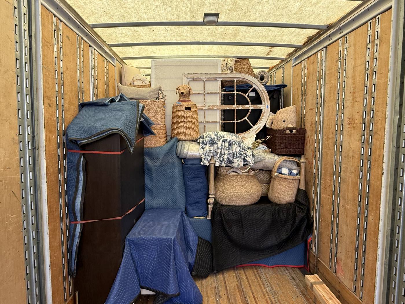 A densely packed moving truck with blanket-wrapped furniture, baskets and a framed mirror strapped in place