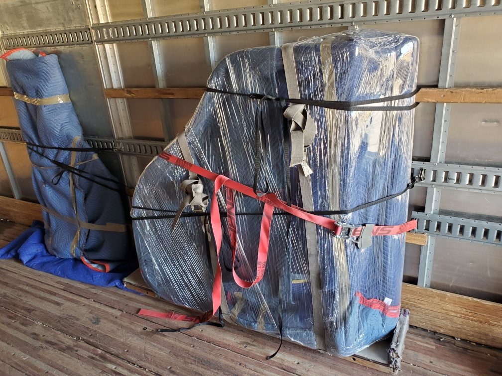 Large blanket-wrapped furniture secured against the truck wall with red ratchet straps